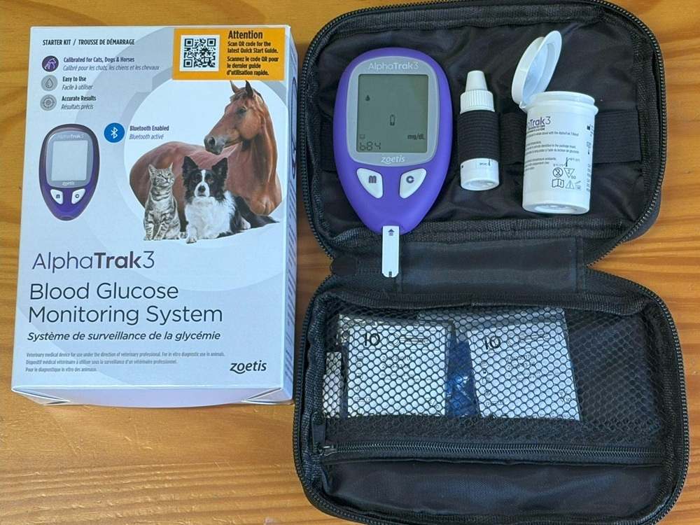 Alpha Trak 3 blood glucose meter kit opened on wood table next to box.
