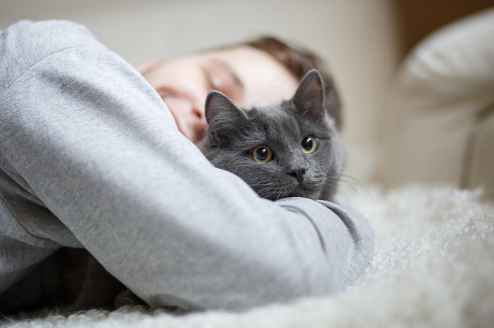 An image capturing a heartwarming scene of a man hugging his cat on a bed.