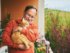Photo of a husband featured with a cat in his arms, illustrating a heartwarming display of companionship and care between a pet owner and his feline friend.
