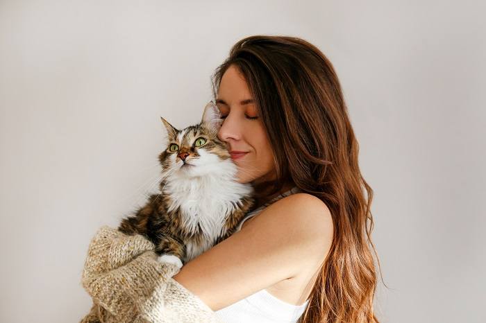 The image portrays a heartwarming scene where a cat is comfortably nestled beside a woman.