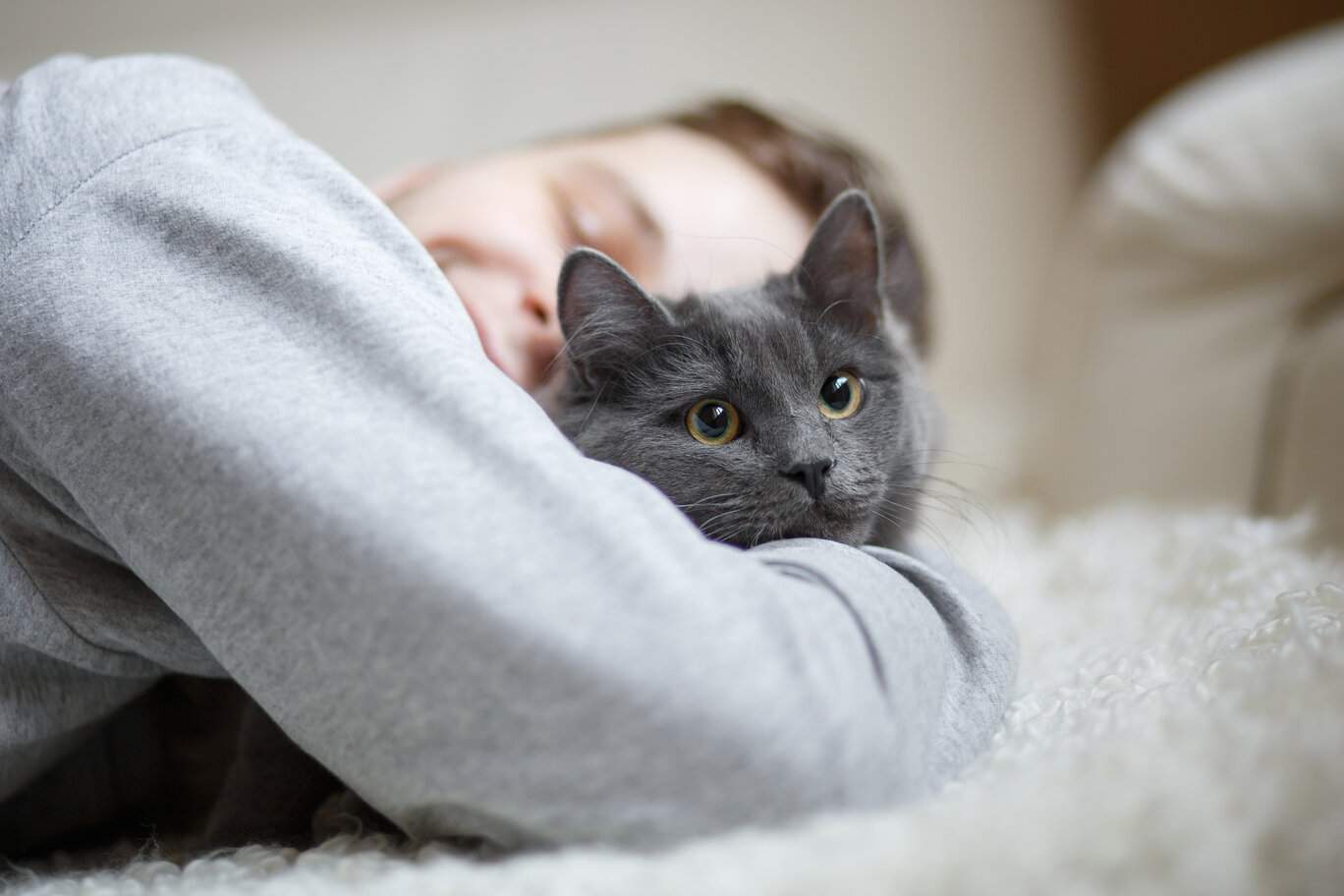 A touching moment unfolds as a man lovingly hugs his cat while they both rest on a bed.