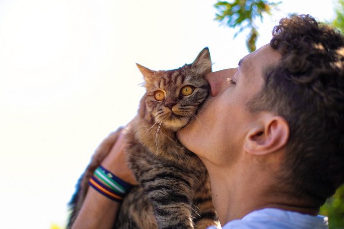 hombre en el jardín abrazando y besando a un gato