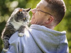 Smiling man carrying his senior tabby cat in the garden
