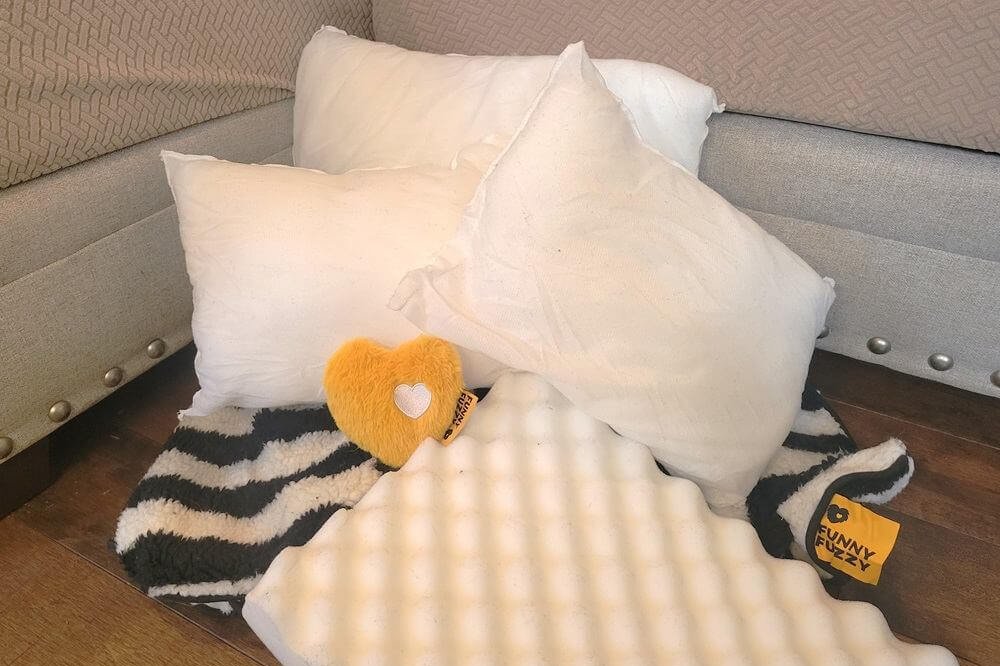 The contents of the FunnyFuzzy shipment include four white pillows, a black and white striped cover, an egg-crate foam pad, and a plush yellow heart toy.